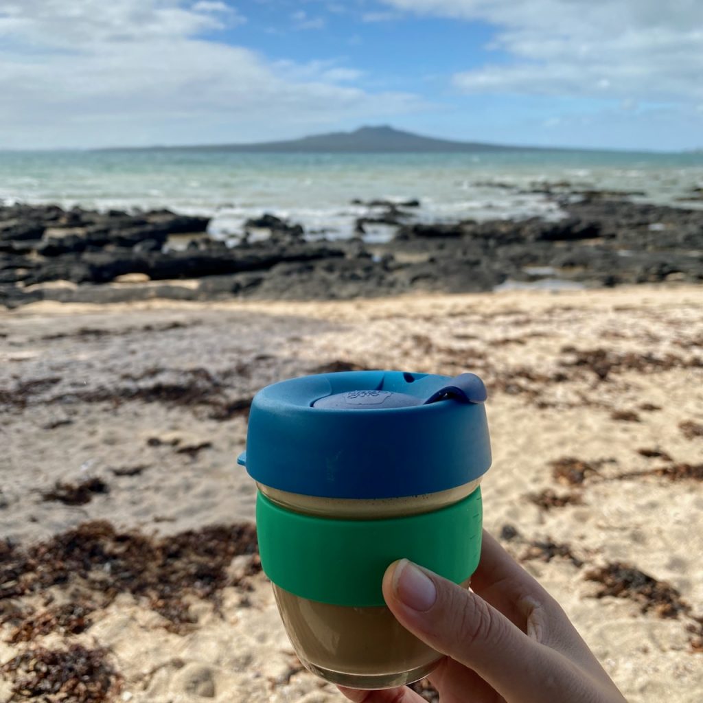 Blue and green keepcup in front of beach