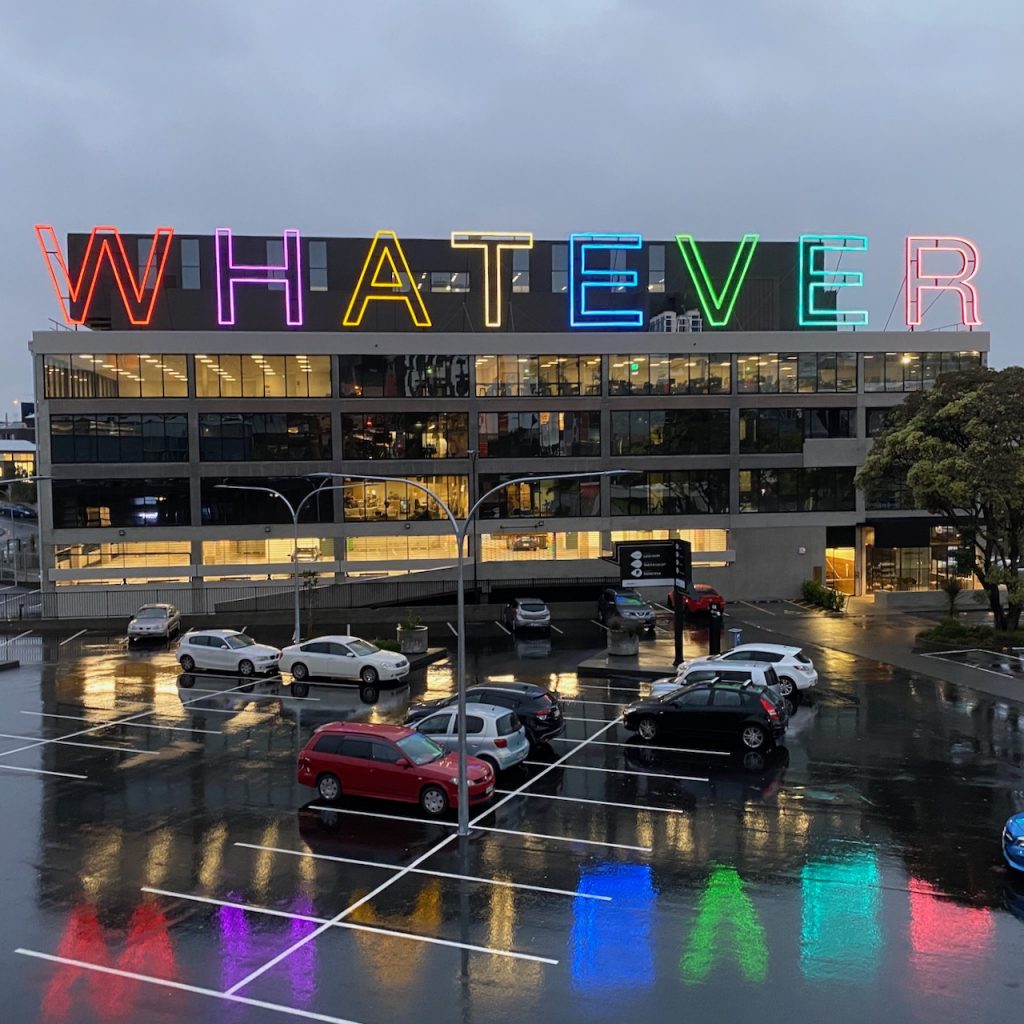 Neon Whatever sign over rainy carpark