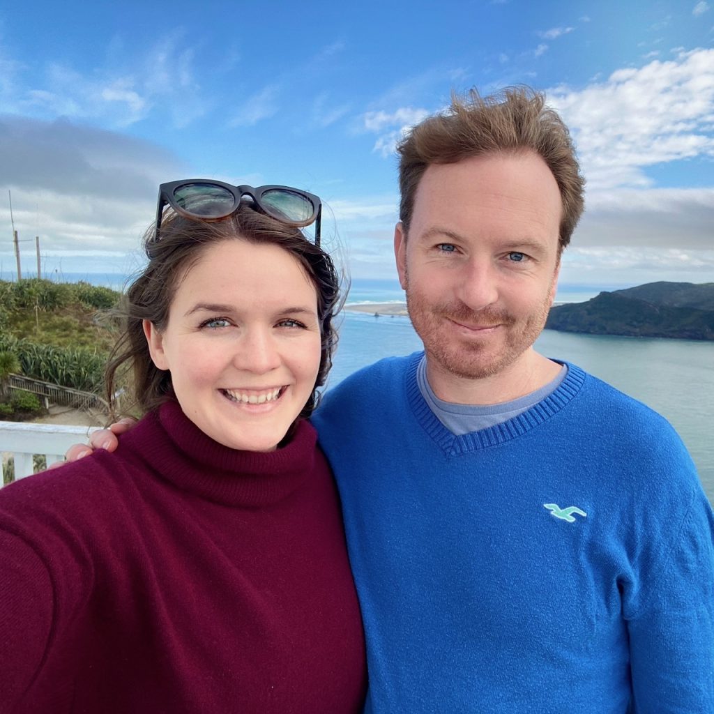 Woman in red jumper and man in blue jumper with sea behind