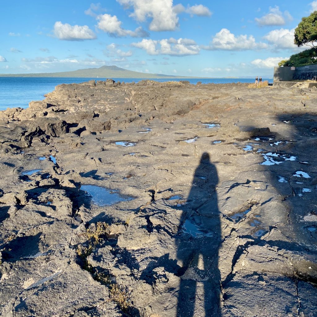 Woman's shadow on rocks with sea in background